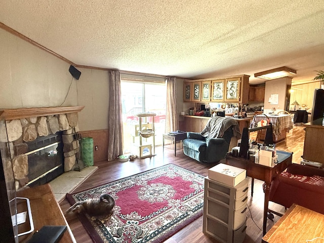 living area with a textured ceiling, wood finished floors, a wainscoted wall, crown molding, and a fireplace