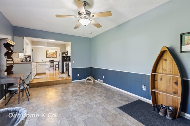 interior space featuring ceiling fan, wainscoting, light stone finish floors, a chandelier, and baseboards