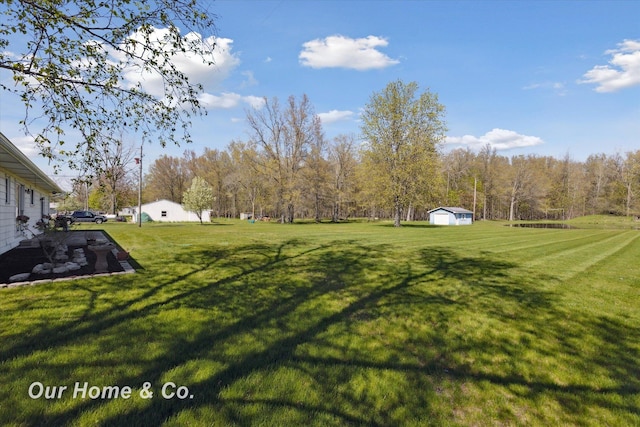 view of grassy yard with an outbuilding, a shed, and a wooded view