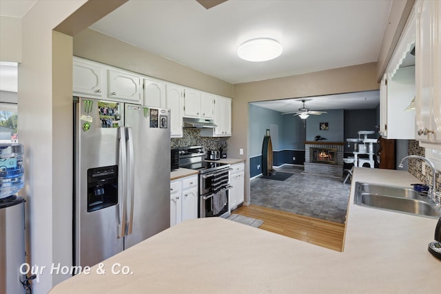 kitchen featuring appliances with stainless steel finishes, under cabinet range hood, a ceiling fan, white cabinetry, and a fireplace