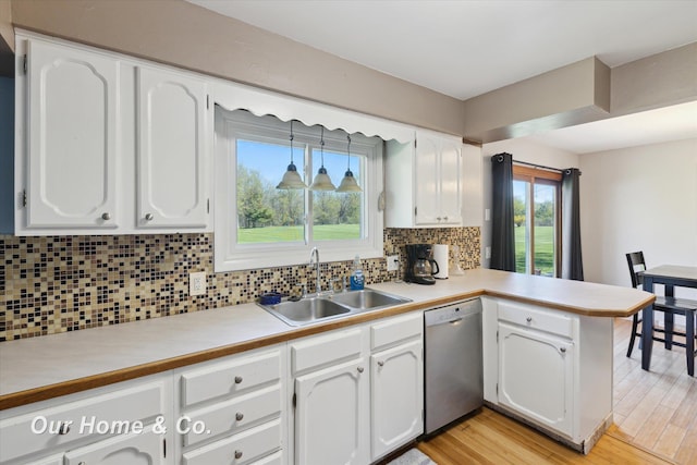 kitchen featuring dishwasher, a sink, a peninsula, white cabinets, and light countertops
