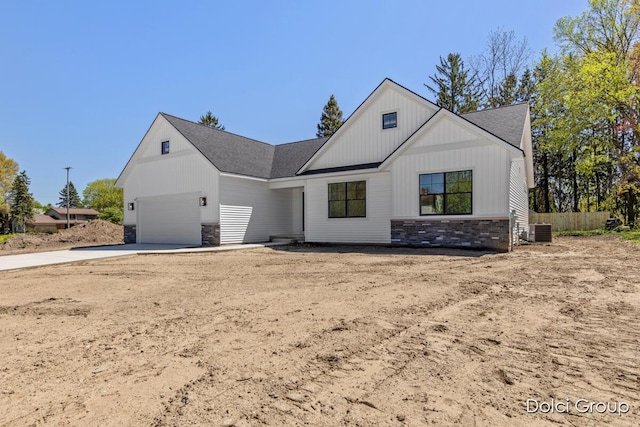 modern farmhouse with stone siding, concrete driveway, a shingled roof, central AC, and board and batten siding