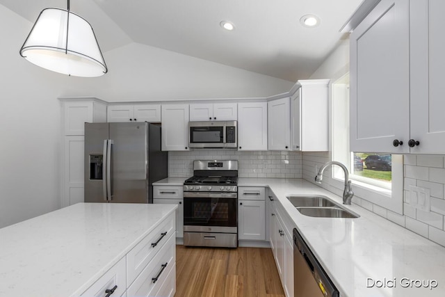 kitchen featuring appliances with stainless steel finishes, a sink, vaulted ceiling, light stone counters, and backsplash