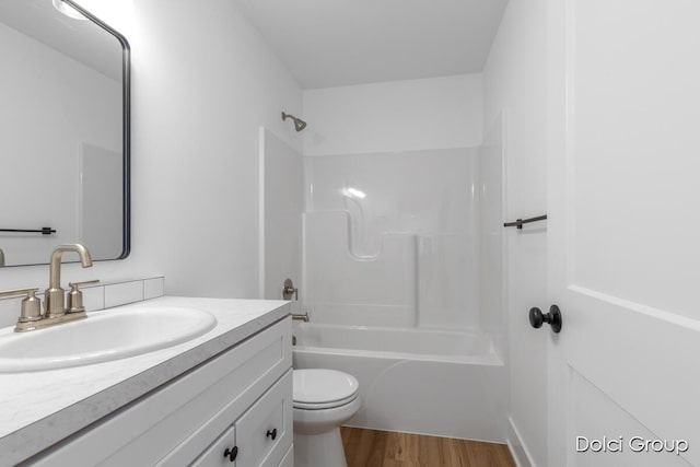 bathroom featuring toilet, wood finished floors, vanity, and shower / washtub combination