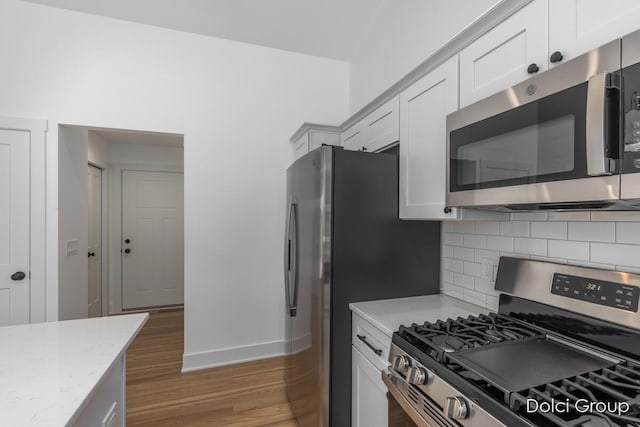 kitchen featuring stainless steel appliances, baseboards, light wood-style floors, tasteful backsplash, and white cabinetry