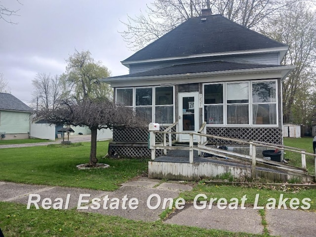 view of front of house with a front yard, roof with shingles, and a sunroom