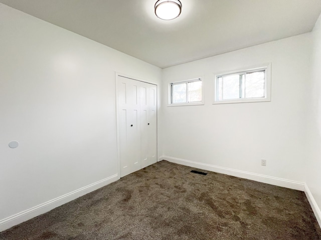 unfurnished bedroom with dark colored carpet, baseboards, and a closet
