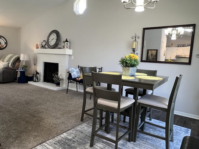 dining room with a chandelier, a brick fireplace, baseboards, and lofted ceiling
