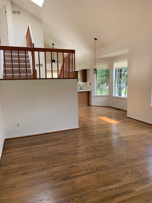 unfurnished living room featuring vaulted ceiling, wood finished floors, a skylight, and baseboards