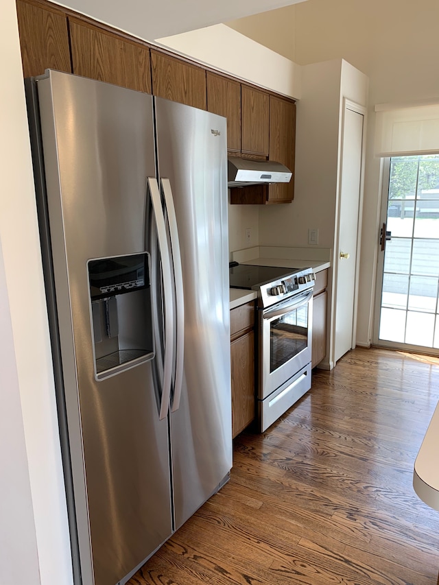 kitchen with appliances with stainless steel finishes, under cabinet range hood, dark wood finished floors, brown cabinetry, and light countertops
