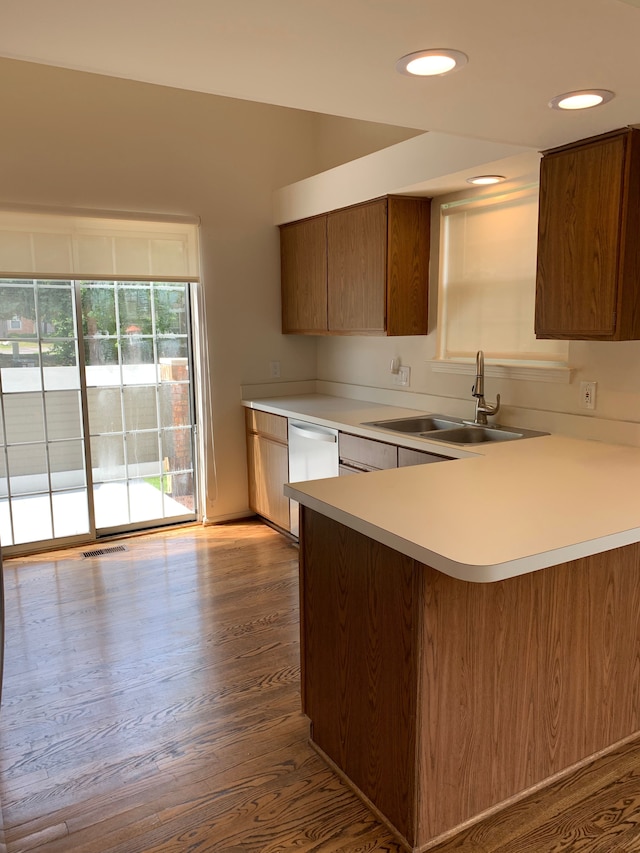 kitchen with a sink, dishwasher, light countertops, wood finished floors, and a peninsula