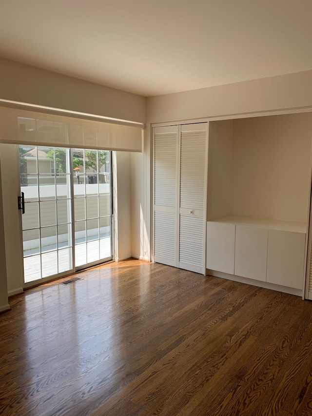 unfurnished bedroom featuring dark wood-style floors, access to outside, and a closet