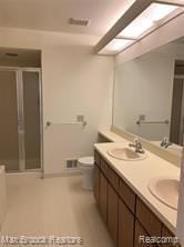 bathroom featuring a stall shower, double vanity, and toilet