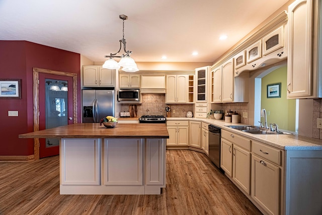 kitchen featuring appliances with stainless steel finishes, a sink, a kitchen island, wood finished floors, and backsplash