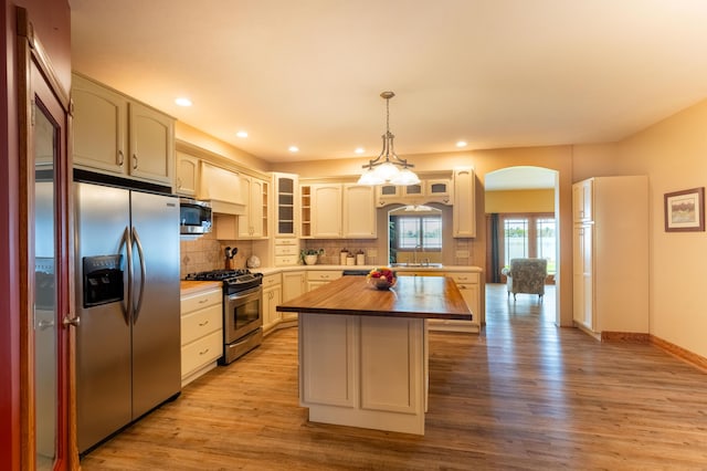 kitchen featuring appliances with stainless steel finishes, a sink, butcher block countertops, a center island, and decorative backsplash