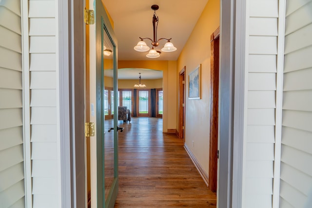 hall with a chandelier, dark wood-style flooring, and baseboards