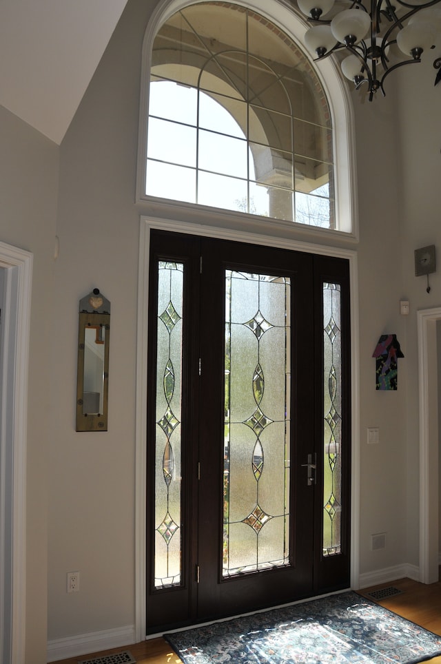 foyer entrance featuring high vaulted ceiling, healthy amount of natural light, wood finished floors, and baseboards