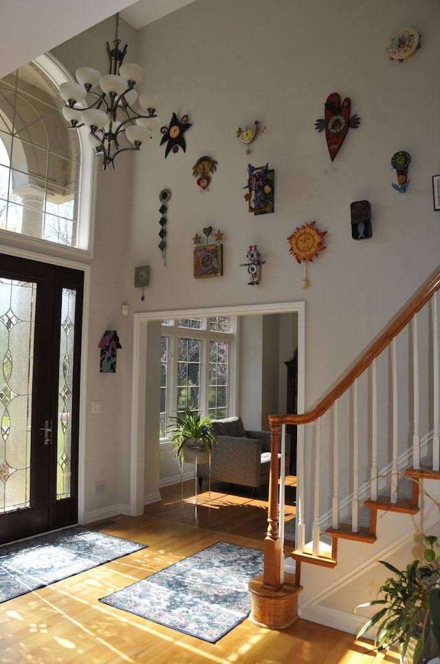 foyer with a towering ceiling, healthy amount of natural light, a chandelier, stairs, and wood finished floors