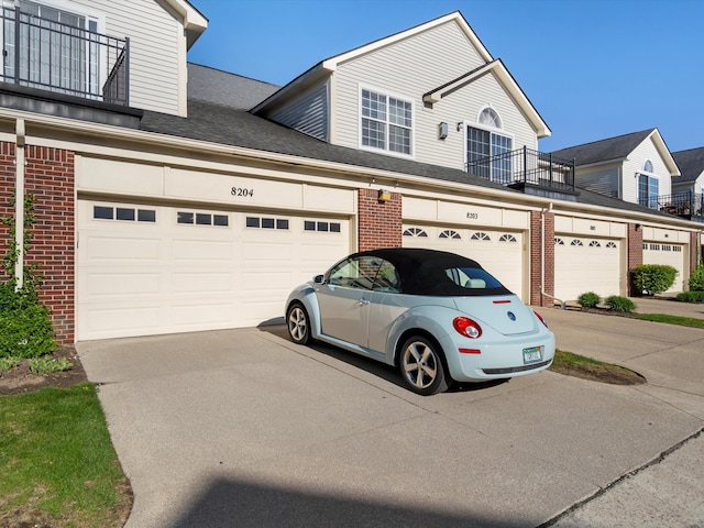 townhome / multi-family property featuring brick siding, a balcony, driveway, and a shingled roof
