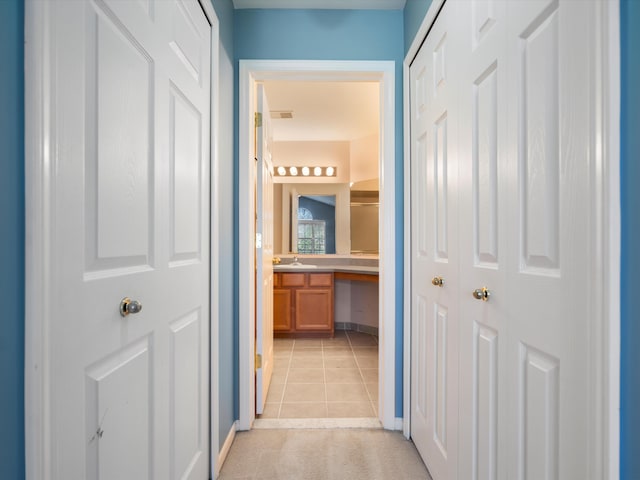 corridor with a sink, light tile patterned flooring, and baseboards