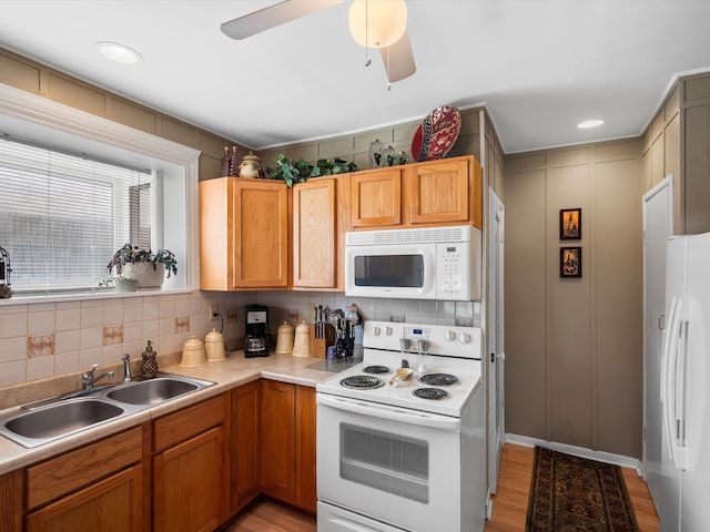 kitchen with white appliances, a sink, decorative backsplash, light wood-type flooring, and light countertops