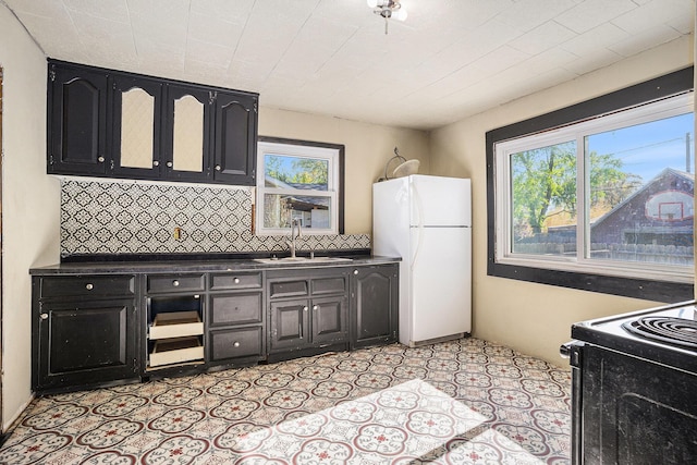 kitchen featuring freestanding refrigerator, a sink, black range with electric cooktop, dark cabinetry, and backsplash