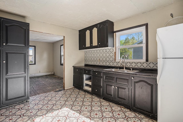 kitchen featuring freestanding refrigerator, a sink, backsplash, and plenty of natural light