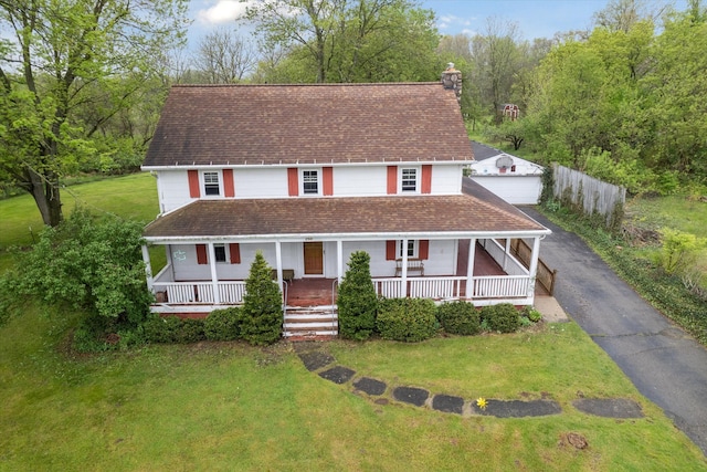 farmhouse inspired home with covered porch, a chimney, a front lawn, and a detached garage
