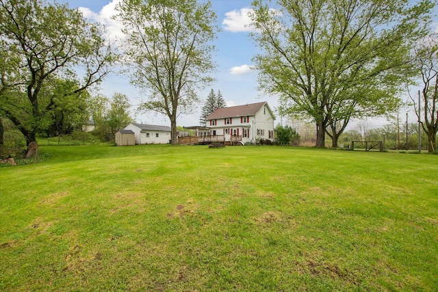 view of grassy yard featuring a storage unit, a deck, and an outbuilding