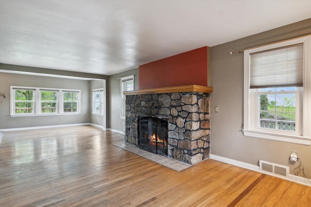 unfurnished living room featuring a stone fireplace, baseboards, and wood finished floors