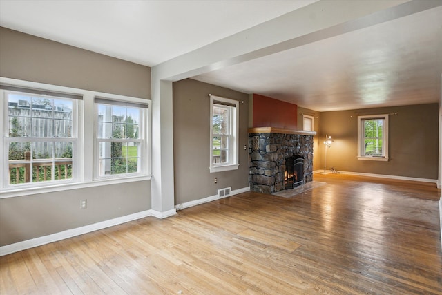 unfurnished living room with hardwood / wood-style flooring, a stone fireplace, and baseboards