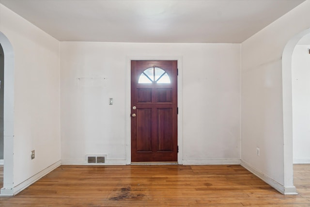 foyer featuring arched walkways, wood finished floors, and baseboards