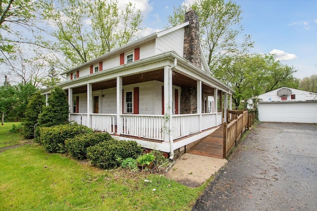 farmhouse inspired home featuring covered porch, a chimney, a garage, an outbuilding, and a front lawn