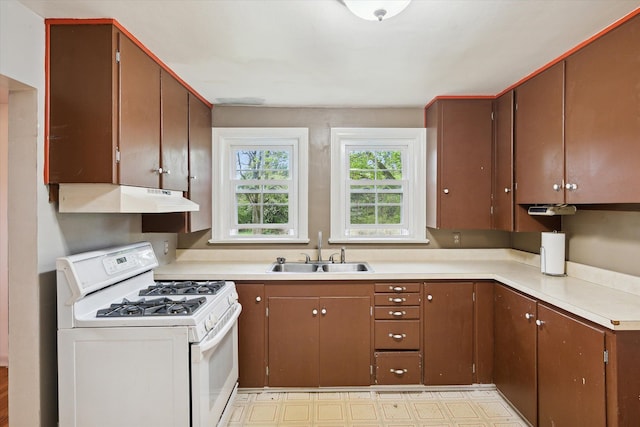 kitchen featuring white gas stove, a sink, under cabinet range hood, light countertops, and light floors