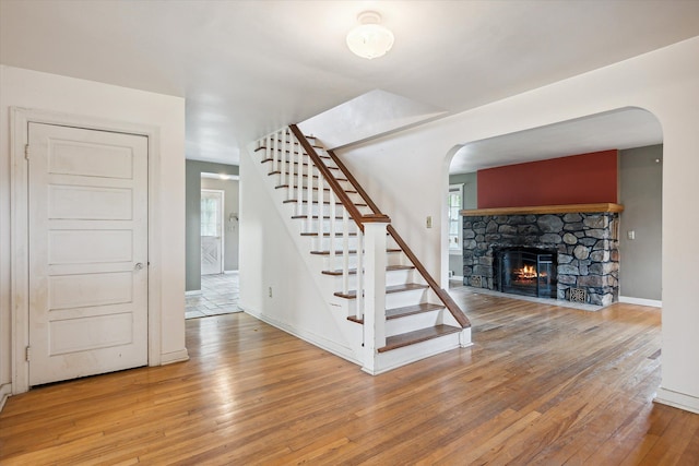 staircase featuring wood-type flooring, arched walkways, a stone fireplace, and baseboards