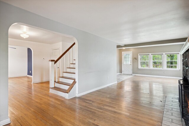 unfurnished living room with arched walkways, wood finished floors, baseboards, and stairway