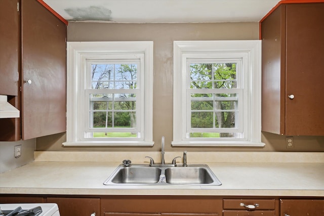 kitchen with a sink, light countertops, brown cabinetry, and wall chimney range hood