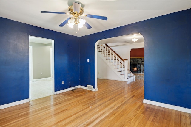 unfurnished room with arched walkways, hardwood / wood-style floors, stairs, a ceiling fan, and baseboards