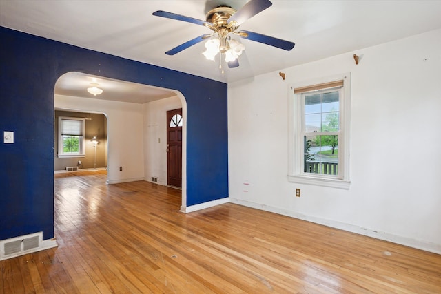 unfurnished room featuring arched walkways, light wood-style flooring, ceiling fan, and baseboards