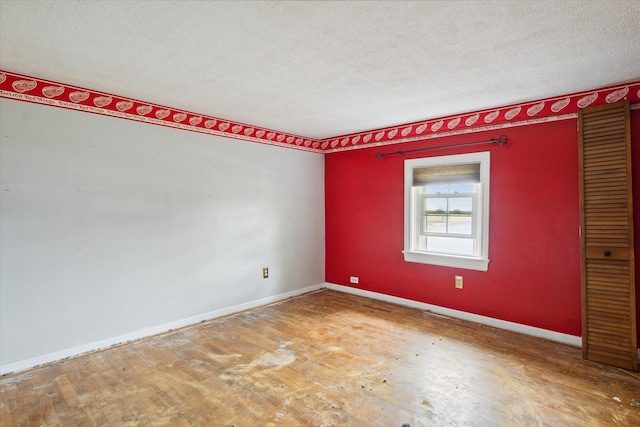 unfurnished room with a textured ceiling, wood finished floors, and baseboards