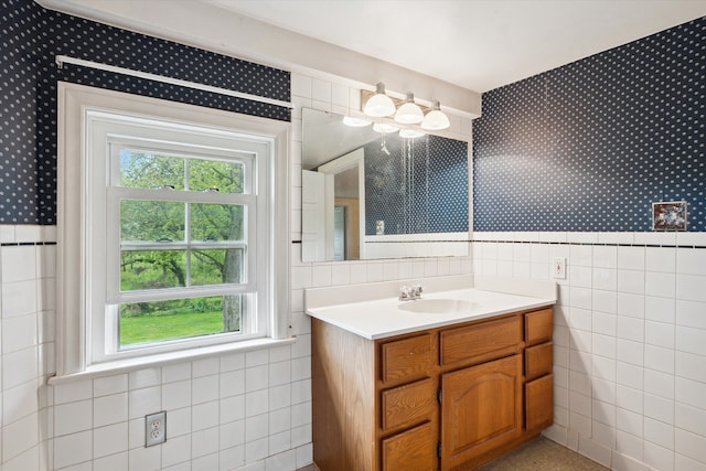 bathroom featuring wallpapered walls, tile walls, healthy amount of natural light, vanity, and a wainscoted wall