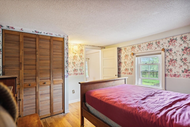 bedroom with wallpapered walls, light wood finished floors, and a textured ceiling