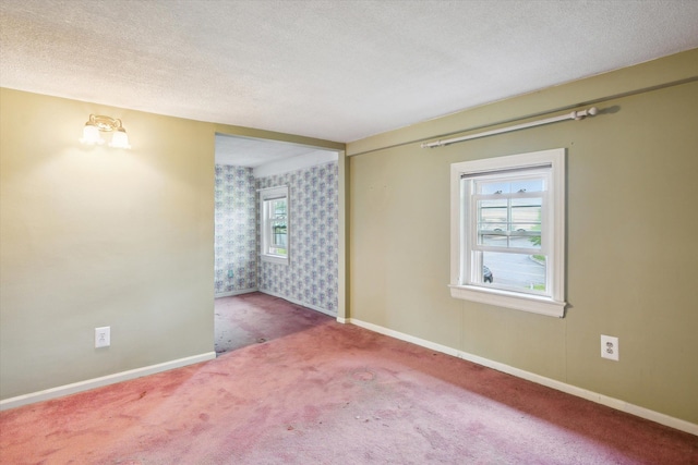 carpeted spare room with wallpapered walls, a textured ceiling, and baseboards