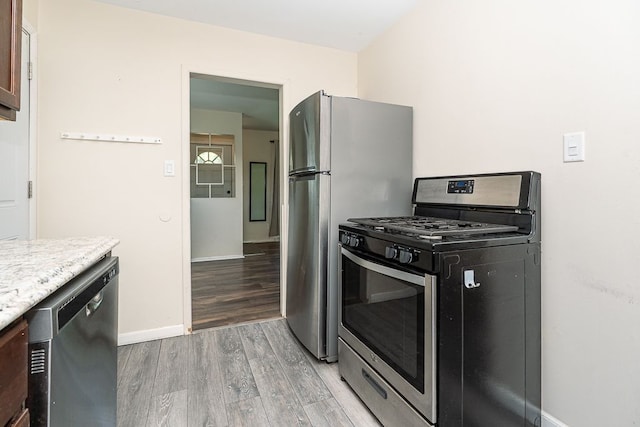 kitchen featuring stainless steel appliances, light wood-type flooring, baseboards, and light stone counters