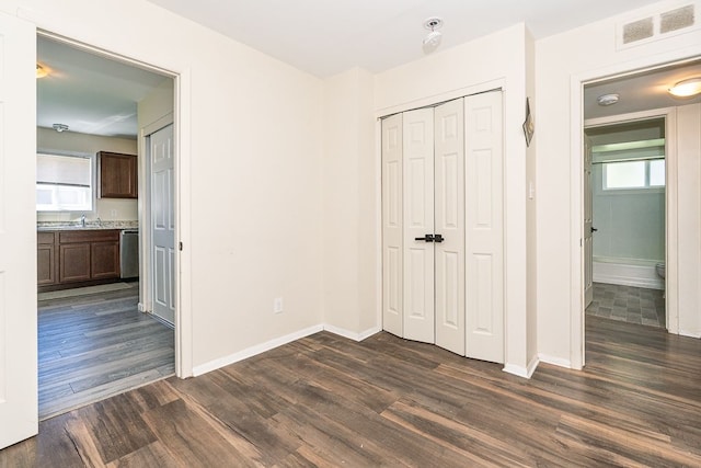 unfurnished bedroom with dark wood-style flooring, baseboards, a closet, ensuite bath, and a sink