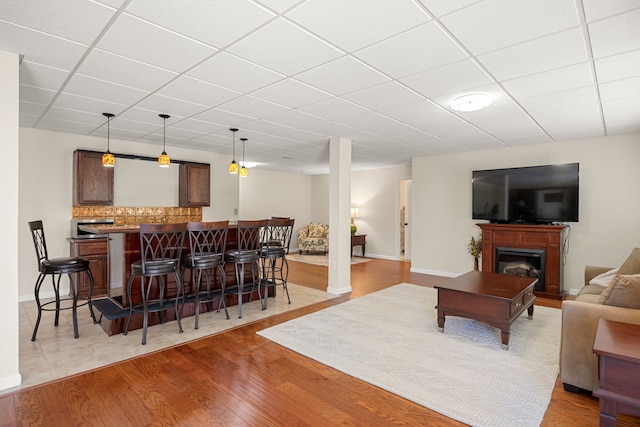 58651 Glacier Club Dr, Washington, MI 48094 - living area with bar area, light wood-style floors, a fireplace, a drop ceiling, and baseboards