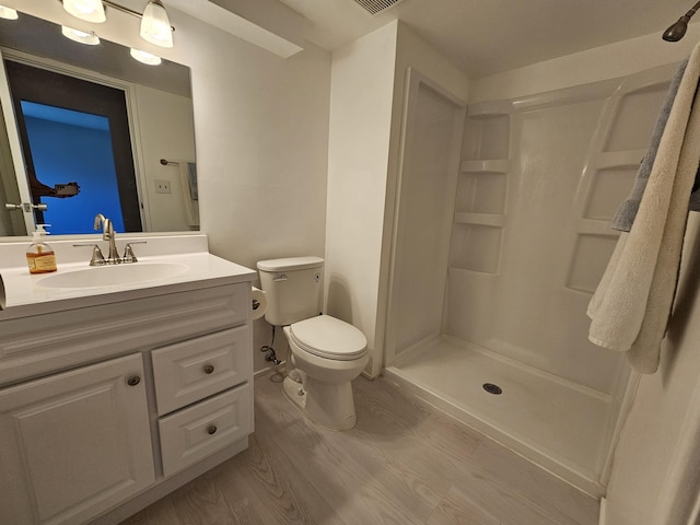 bathroom featuring wood finished floors, a shower stall, toilet, and vanity