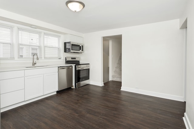 kitchen with appliances with stainless steel finishes, a sink, baseboards, dark wood-style floors, and light countertops