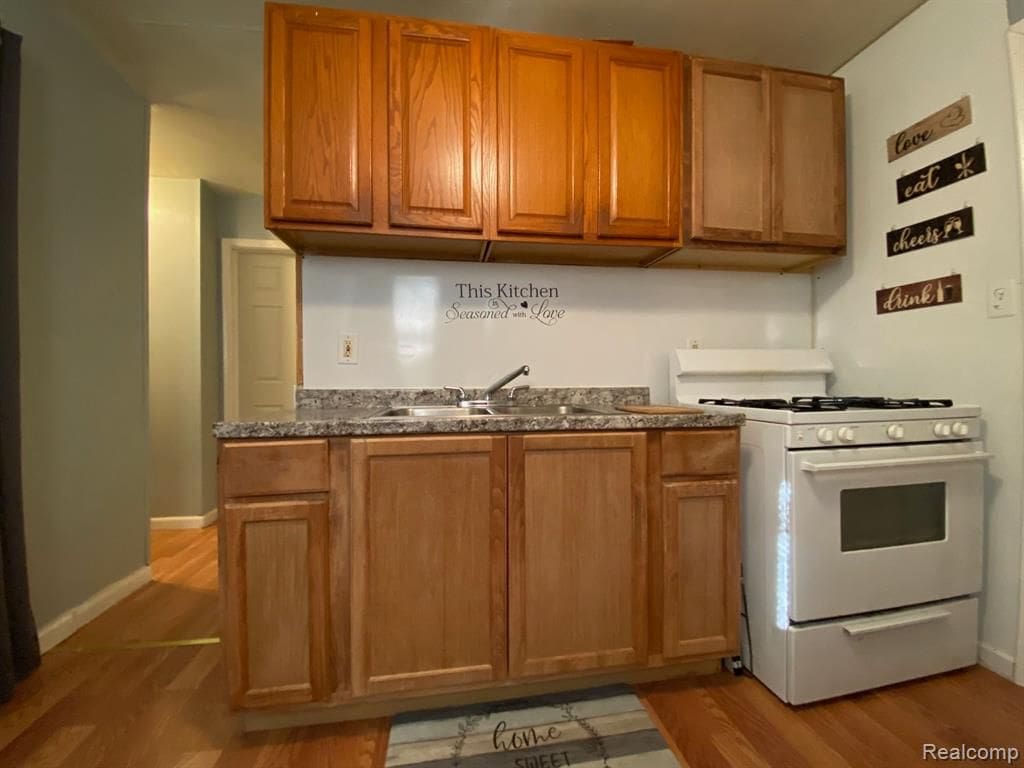 11107 Hudson Ave, Warren, MI 48089 - kitchen with white gas range oven, a sink, dark countertops, light wood-style flooring, and brown cabinetry