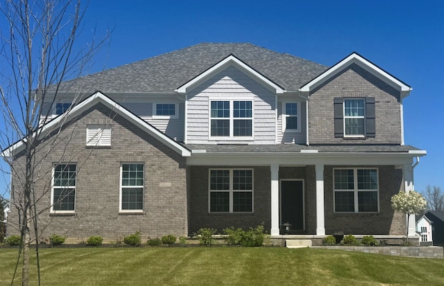view of front of property featuring a front yard, brick siding, covered porch, and roof with shingles
